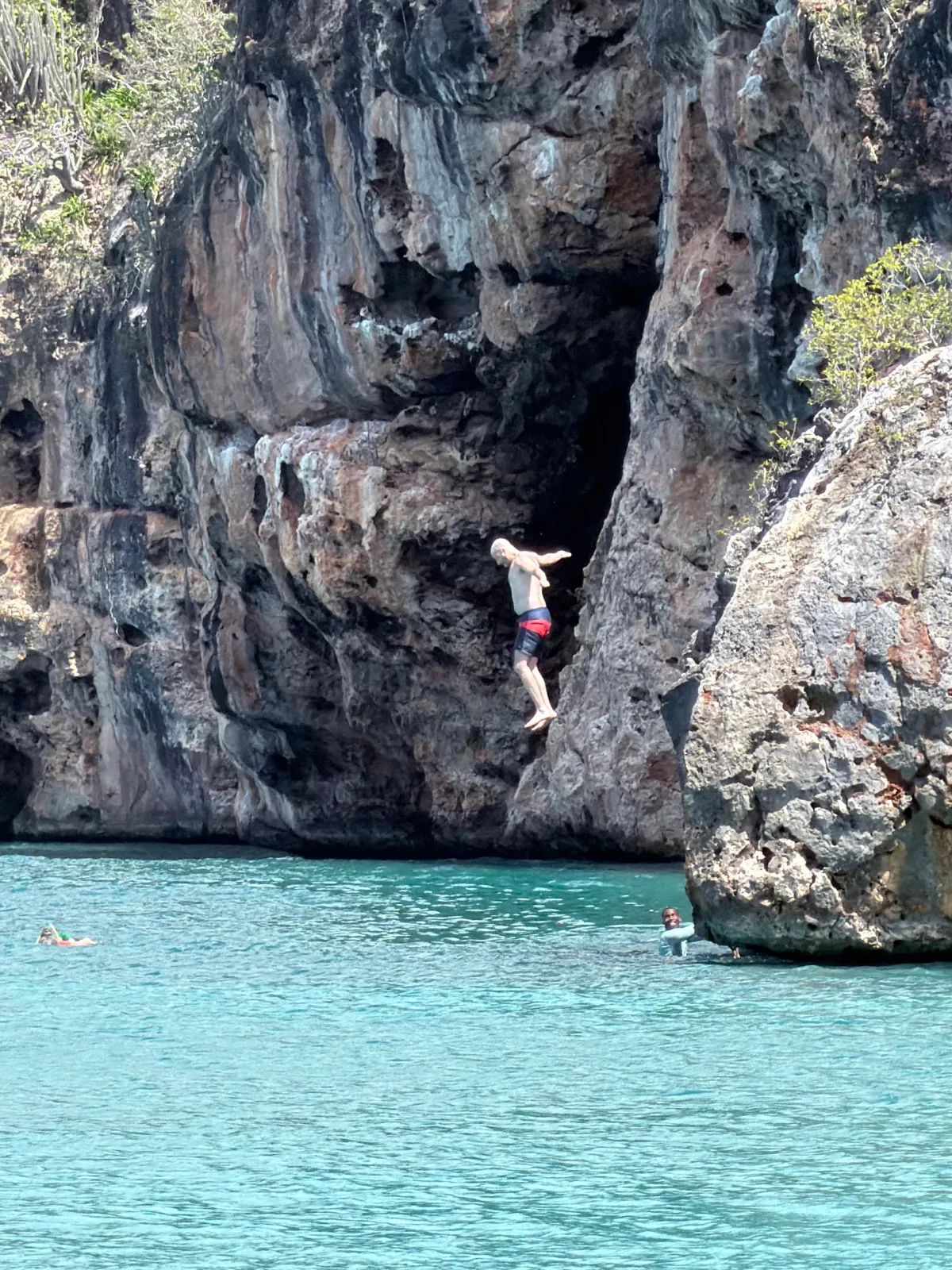 A guest leaping from the limestone cliffs into the turquoise water at the snorkel stop