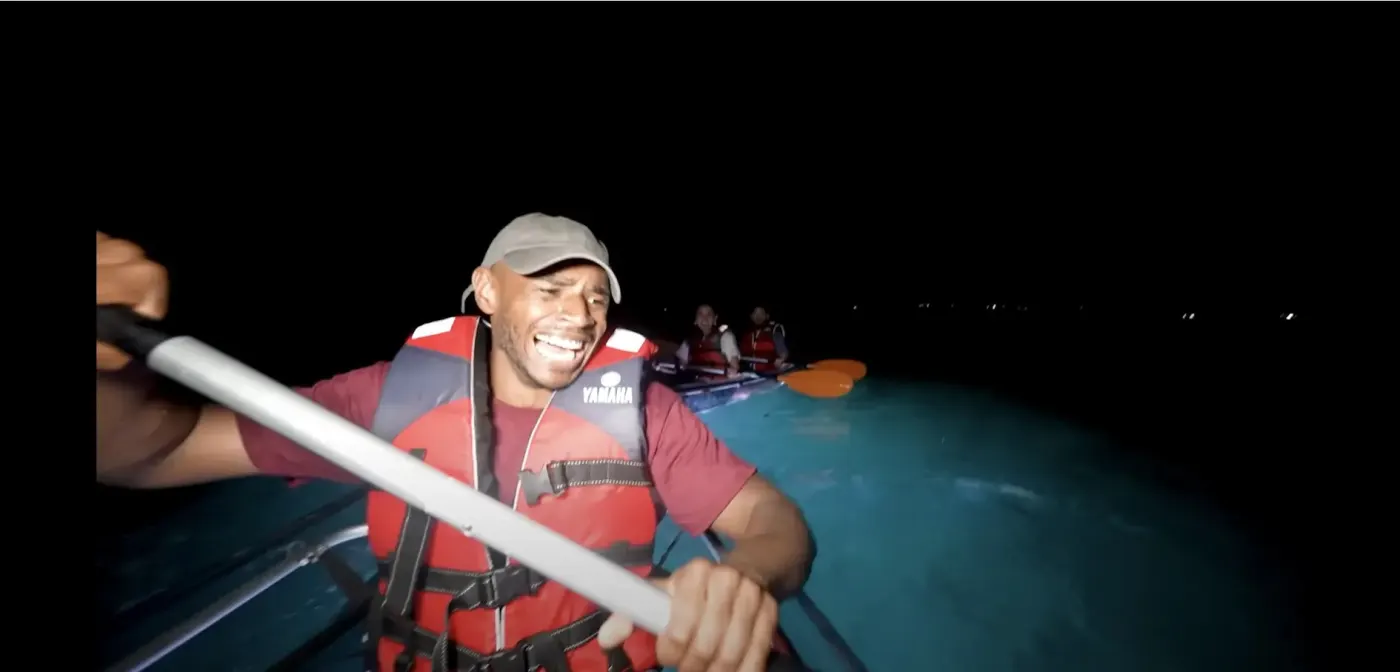 TFIL crew member grinning mid-paddle in an LED-lit clear kayak after dark