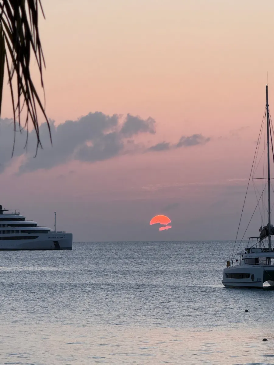 A red sun setting between a yacht and a catamaran